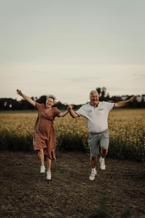 An older couple walking hand in hand through a summer field at dusk